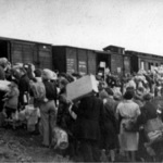 Mensen staan bepakt en bezakt te wachten bij de goederenwagons van een trein in doorvoerkamp Westerbork